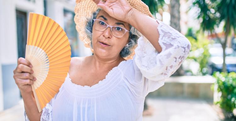 Old woman fanning herself under hot weather.