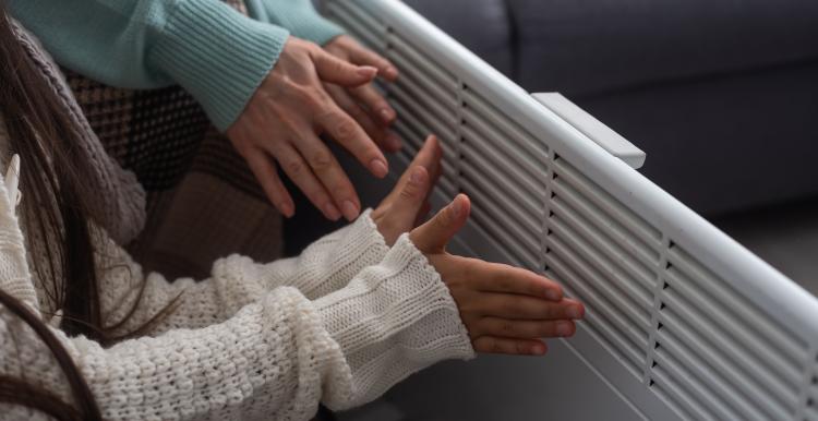 Family warming hands near electric heater at home, closeup