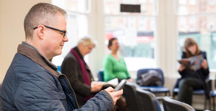 Share your views A man in a hospital waiting room looking at his phone