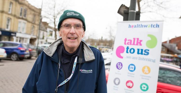 A man standing outside in front of a Healthwatch sign