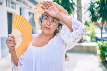 Old woman fanning herself under hot weather.