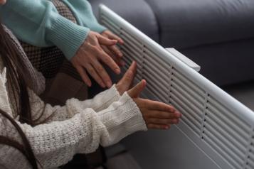 Family warming hands near electric heater at home, closeup