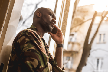 Man looking out at window, listening to phone call.