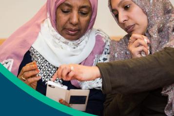 Two muslim women - a woman in a hijab guiding her on how to navigate the website on her phone.