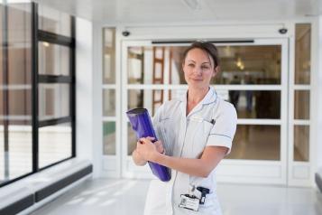 A nurse in a hospital corridor holding a folder and smiling