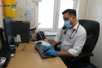 Image of GP at his desk on the phone and typing on his computer simultaneously