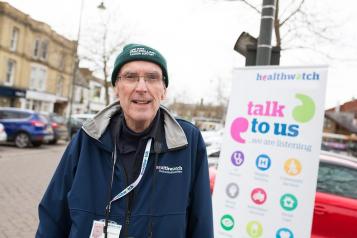 A man standing outside in front of a Healthwatch sign
