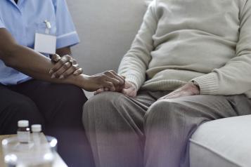 A nurse holding an old man's hand on the sofa