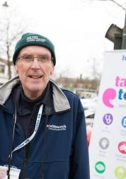 A man standing outside in front of a Healthwatch sign